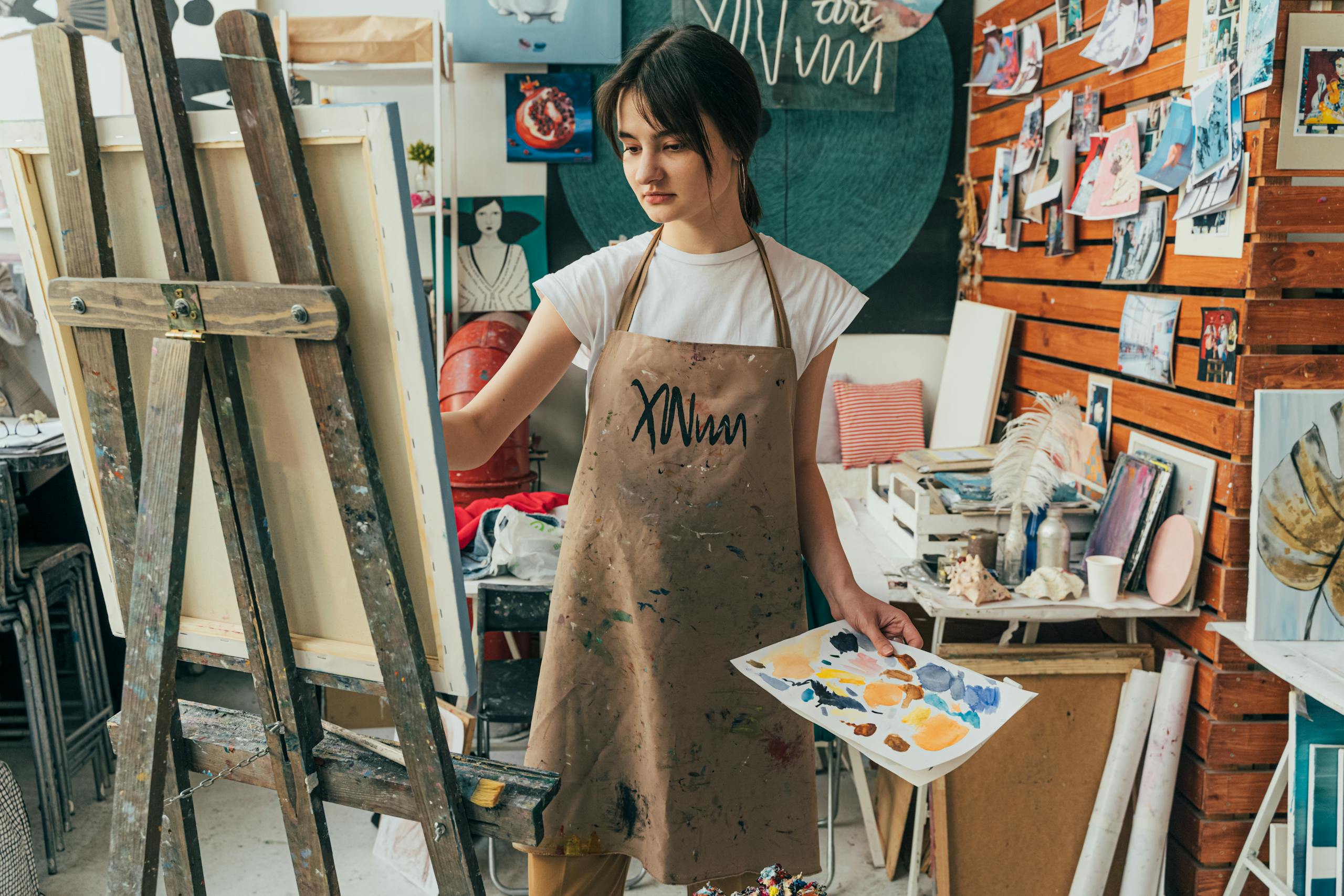 A young woman artist painting on canvas in a vibrant art studio, surrounded by creative artworks.