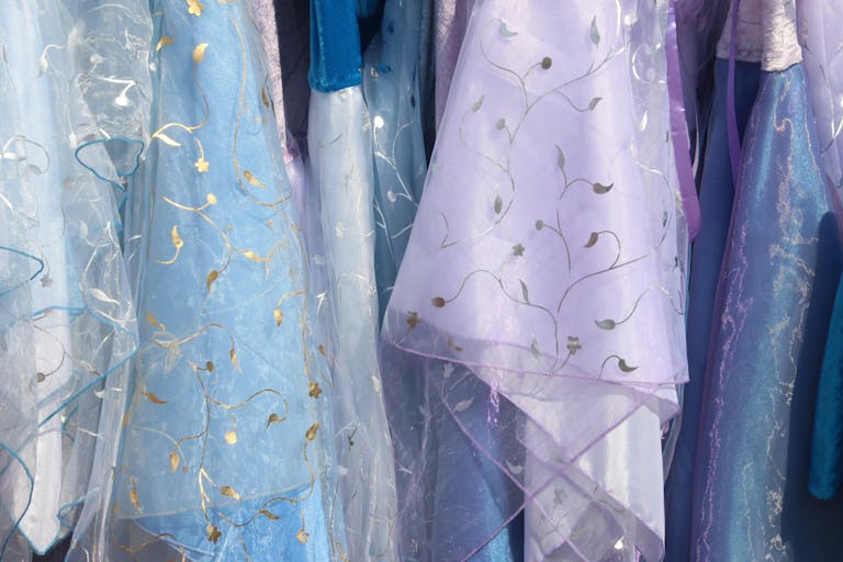 Close-up of pastel-colored dresses with intricate floral patterns and shiny fabrics.