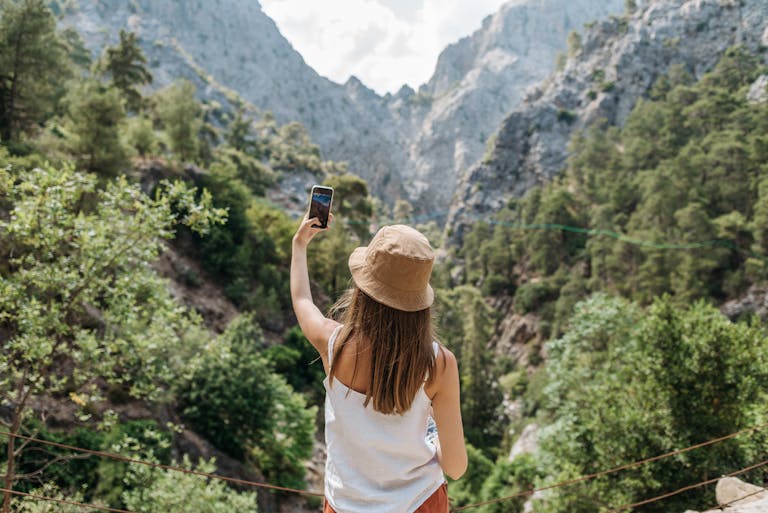 Young woman taking a selfie in a mountainous outdoor setting, enjoying nature and hiking.